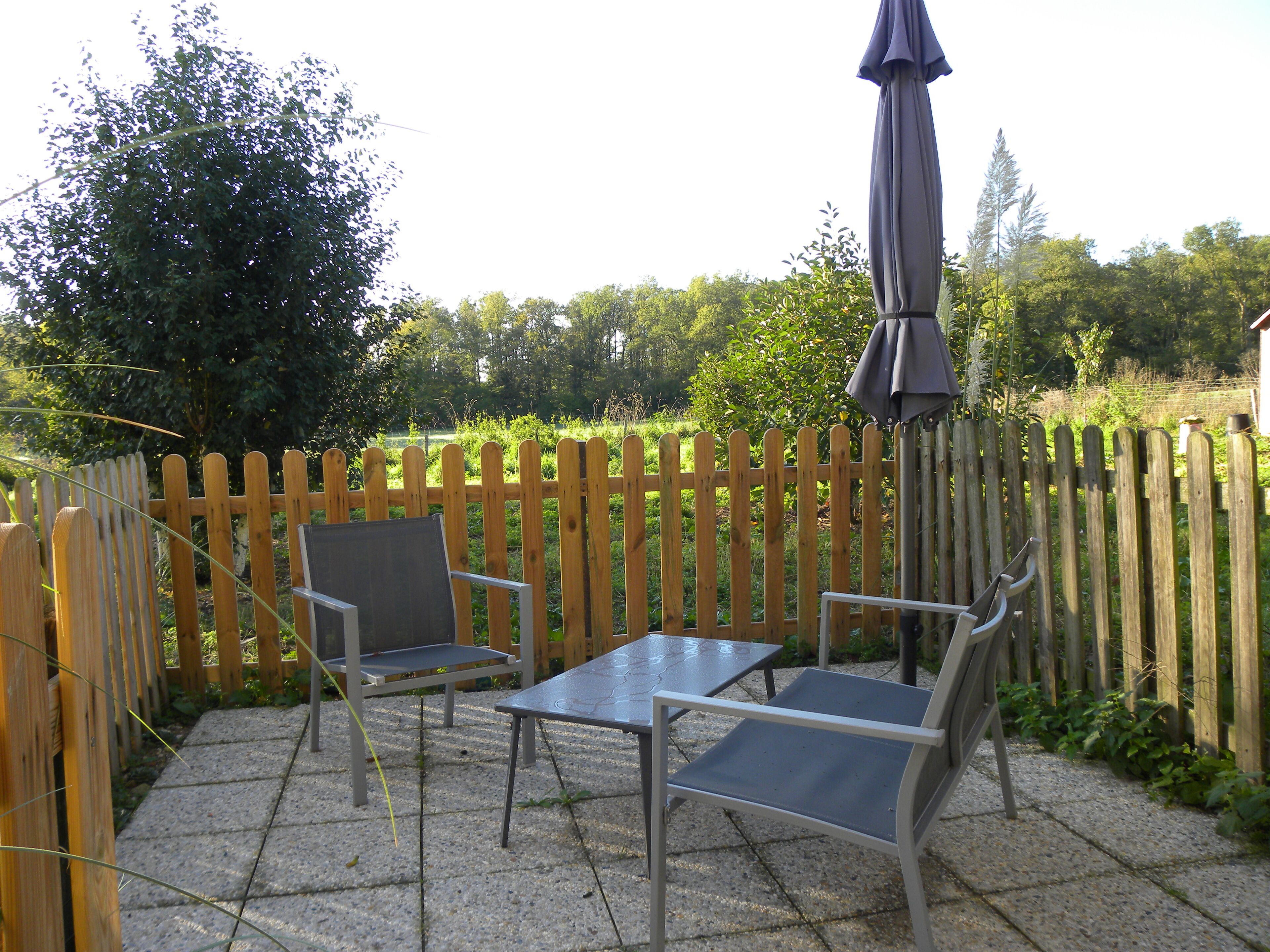 Un patio con dos sillas de metal y una mesa, una cerca de madera y un paraguas.