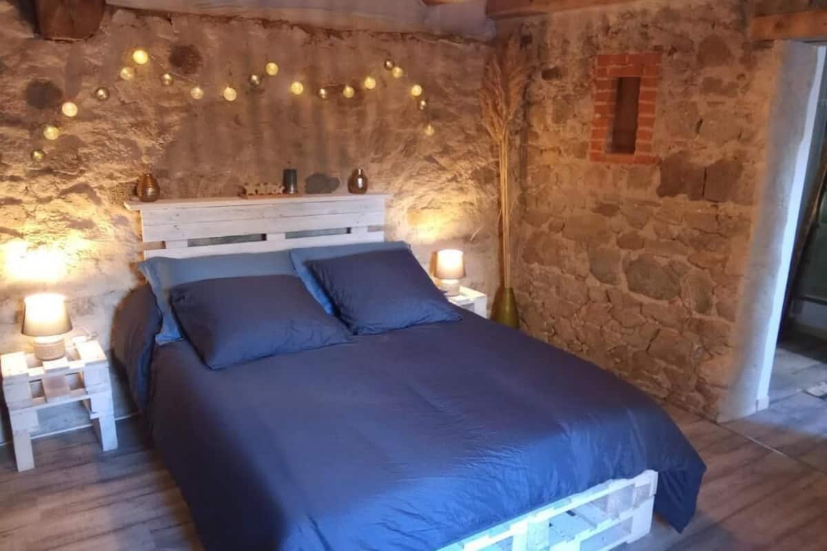 A bed with a white frame, two white nightstands, and a stone wall.