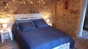 A bed with a white frame, two white nightstands, and a stone wall.
