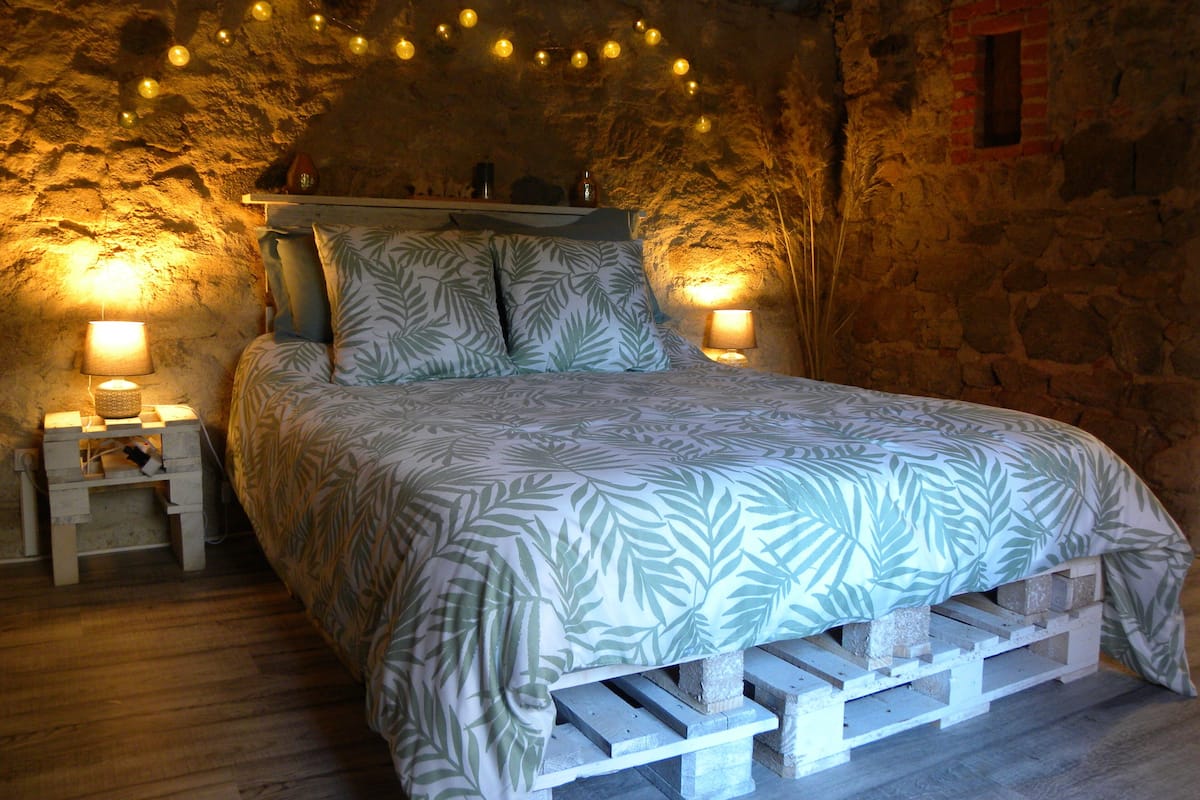 A bed with a leaf-patterned bedspread, two bedside lamps, and a string of lights on the wall.