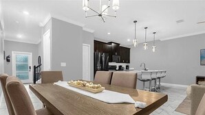A modern dining area with a wooden table, cushioned chairs, and a chandelier. - Last Minute Disney Getaway! Townhouse with Private Pool. Book Now! #149357 (Orlando)