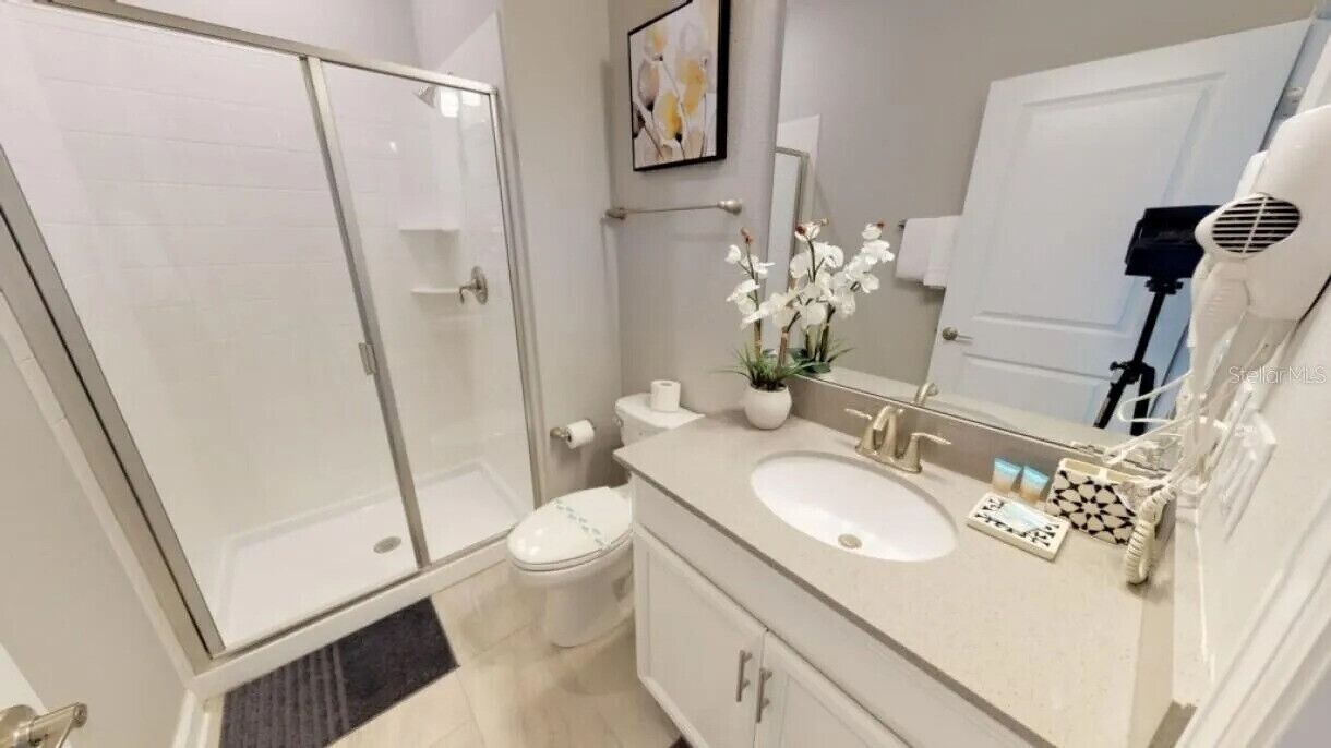 A modern bathroom with a glass shower enclosure, a toilet, a sink with a vanity, and a mirror.