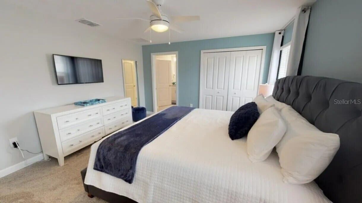 Un dormitorio con cama, cómoda, televisor y ventilador de techo.