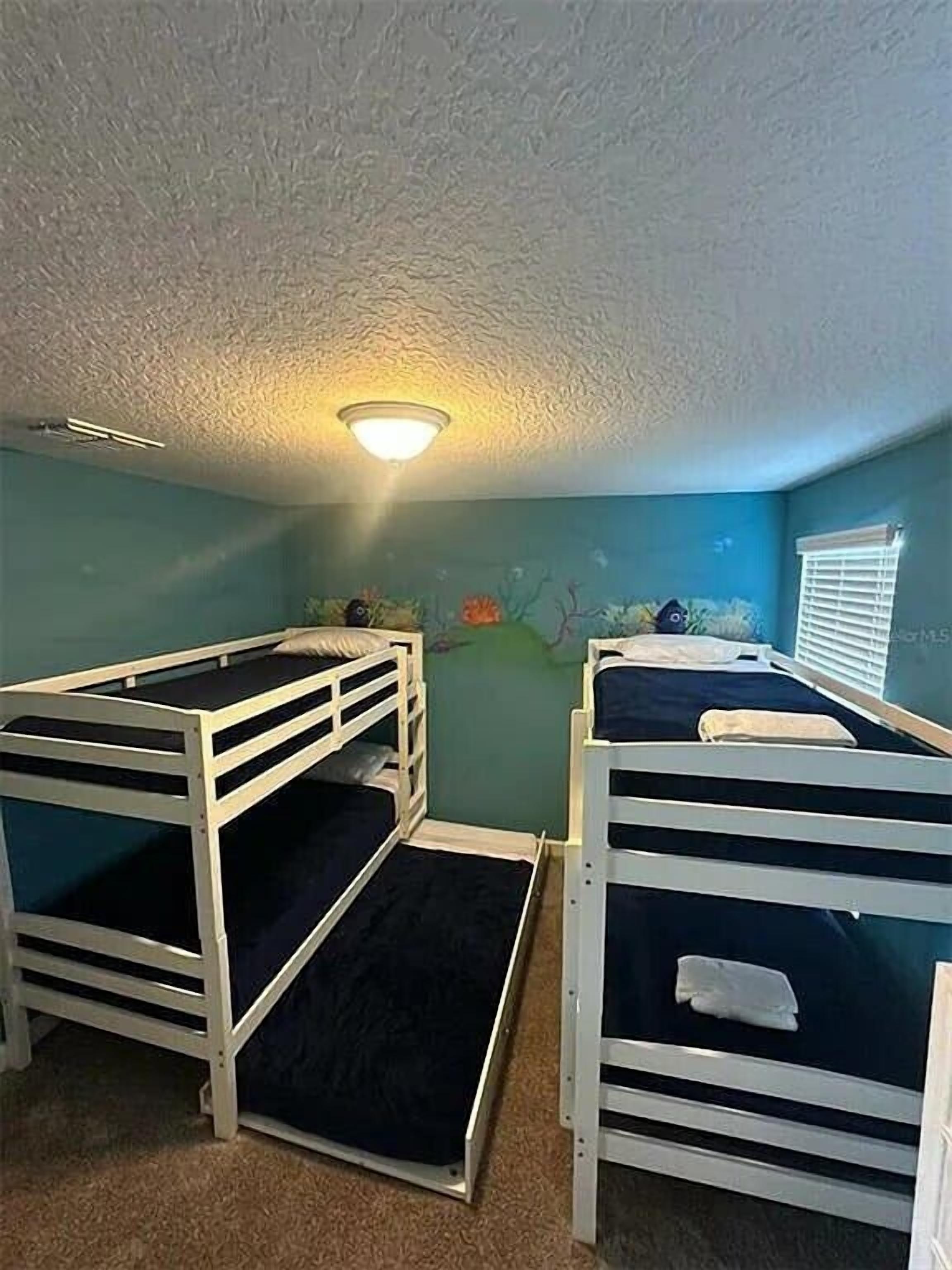 A room with bunk beds, a ceiling light, and a window with blinds.