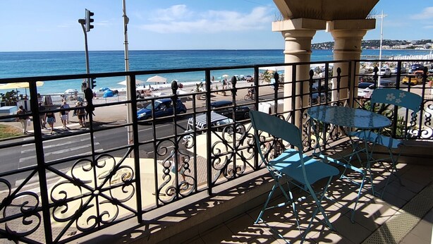 A balcony with a view of the beach and ocean, featuring a metal railing and blue chairs. - Charming three-room beachfront apartment with stunning sea views in the heart of Menton (Menton)