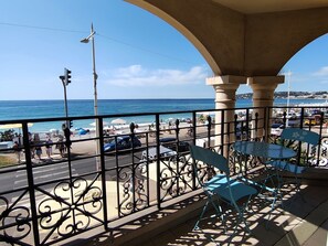 A balcony with a view of the beach and ocean, featuring a metal railing and blue chairs. - Charming 3-room apartment on the waterfront with a splendid ocean view in the heart of Menton (Menton)