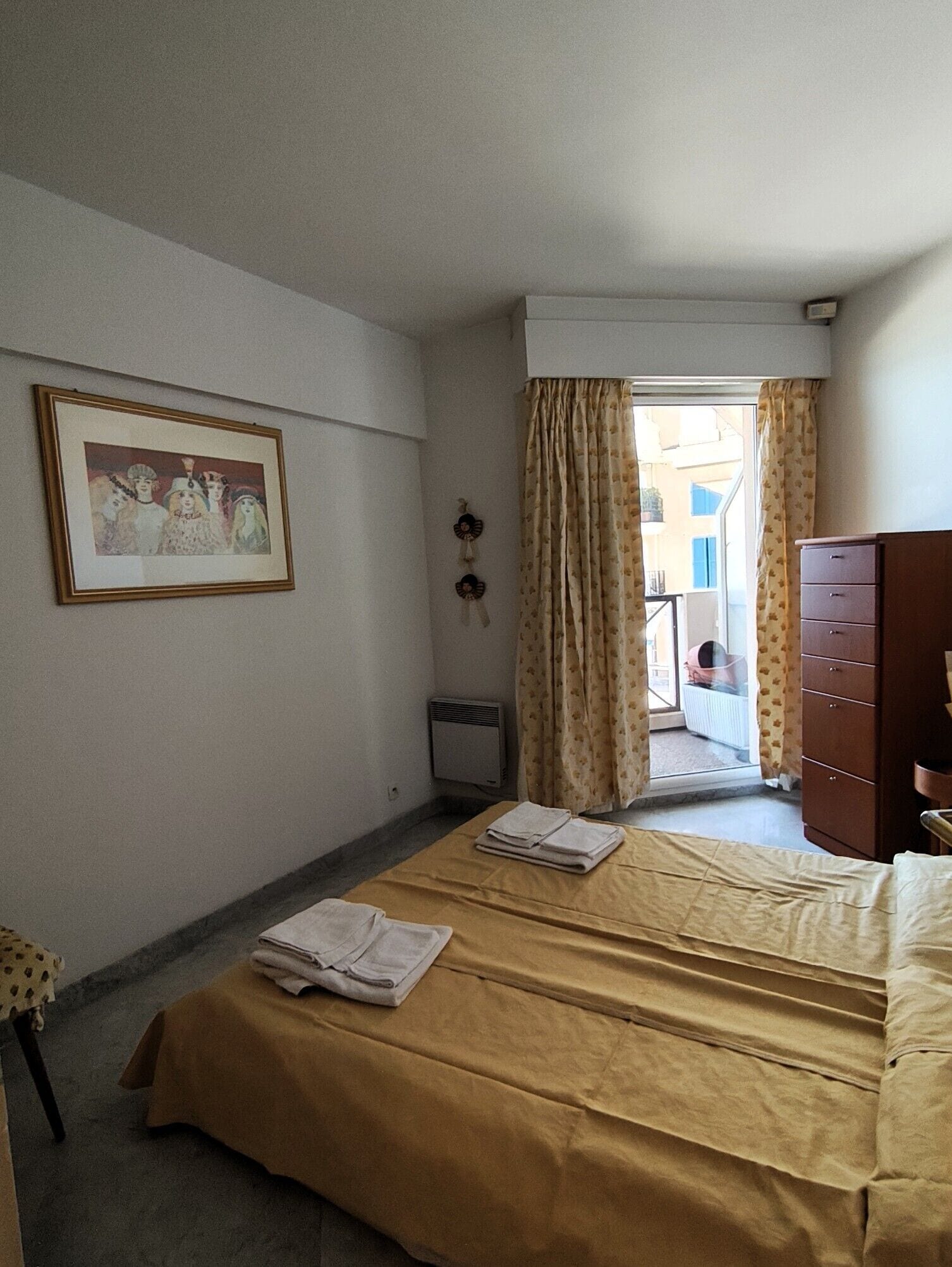 A hotel room with a bed, a dresser, a radiator, and a window with curtains.