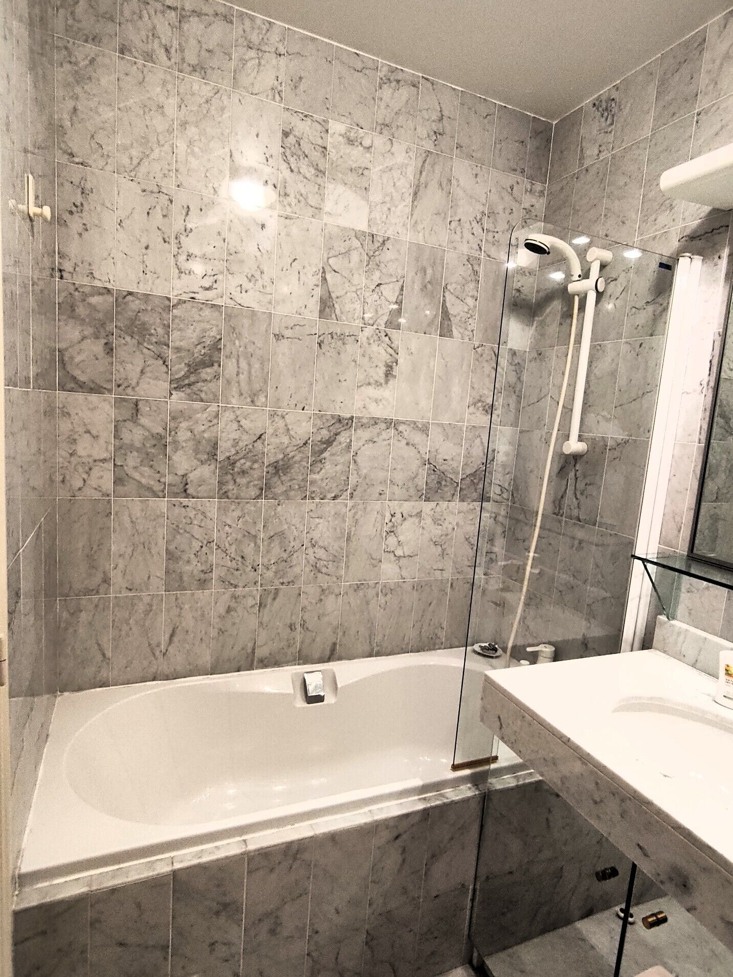 A bathroom with a bathtub, a glass shower enclosure, and a marble-tiled wall.