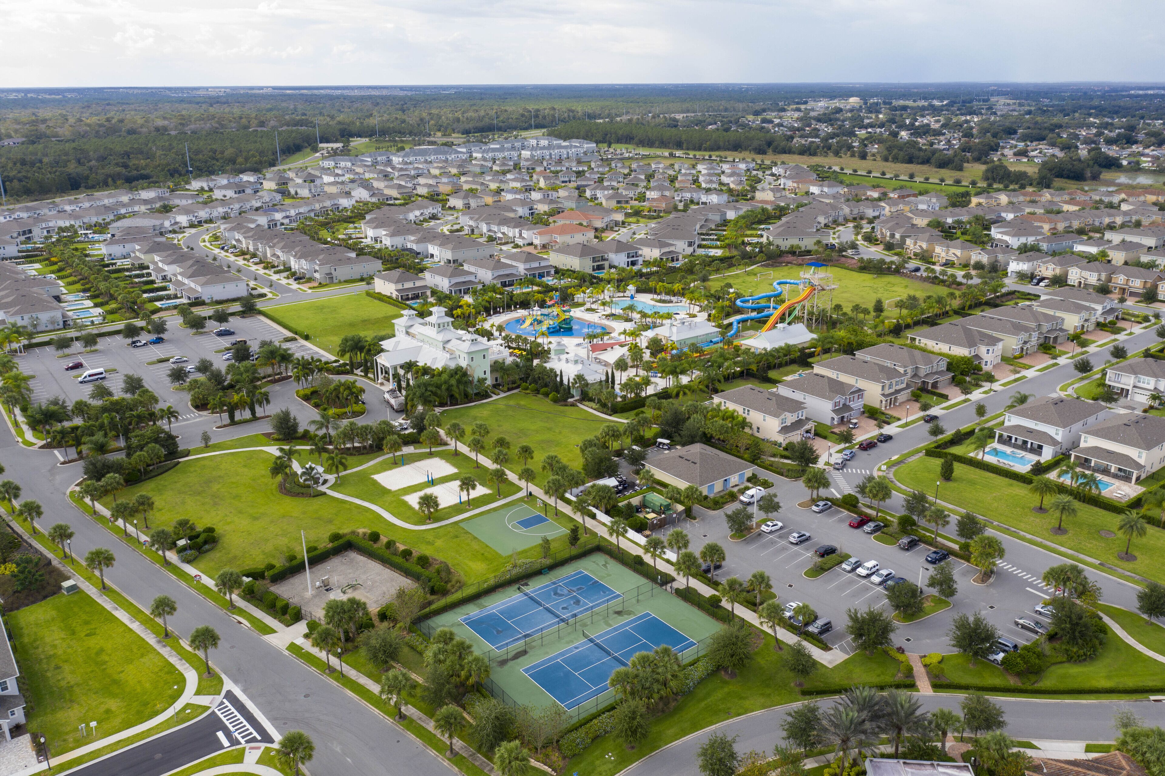 An aerial view of a residential area with houses, a swimming pool, tennis courts, and a playground.