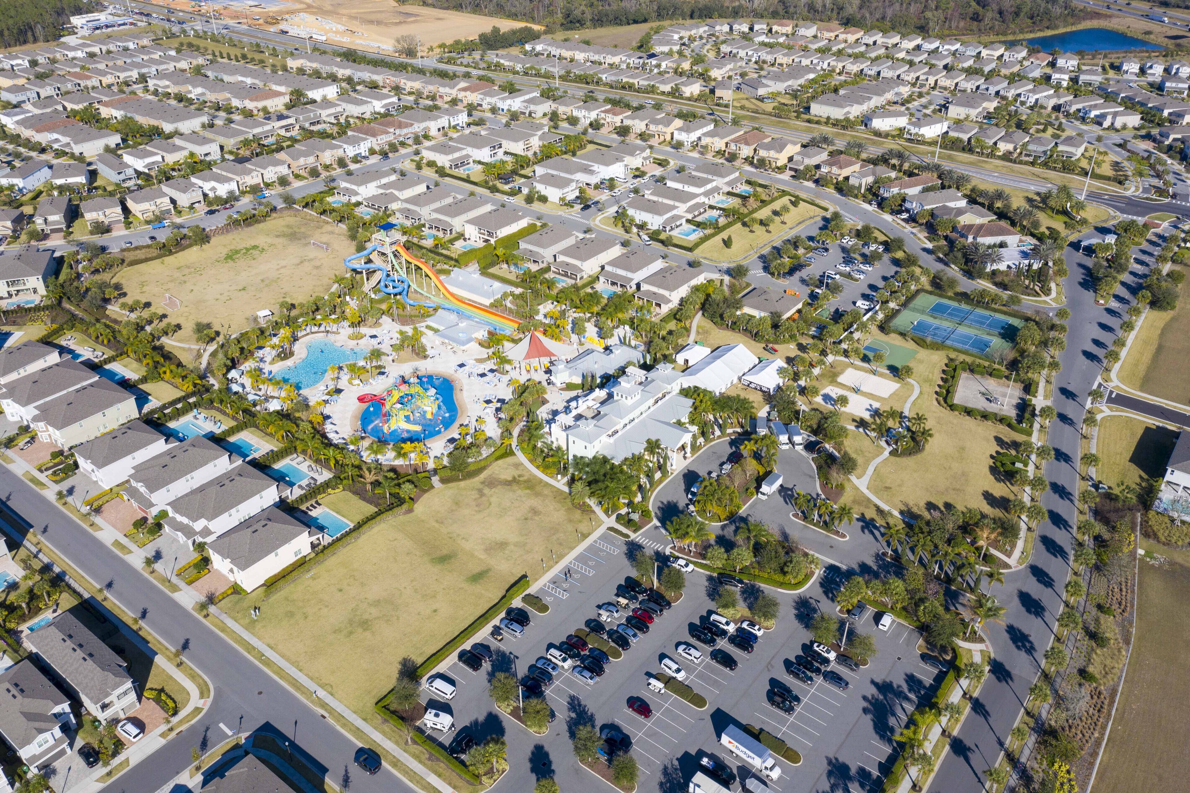 An aerial view of a residential area with a central park featuring a playground, tennis courts, and a swimming pool.