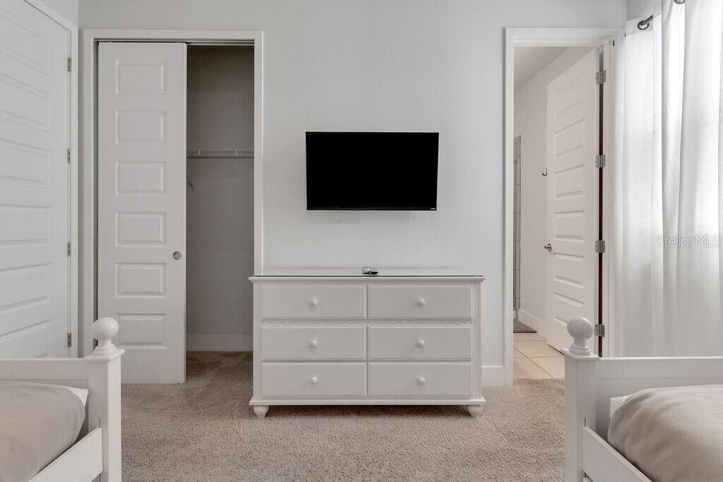 A bedroom with a white dresser, a television mounted on the wall, and a closet with a door open.
