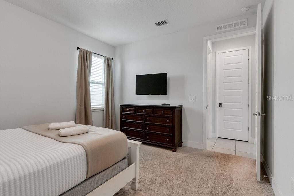 Une chambre à coucher avec un lit, une commode, un téléviseur et une porte.
