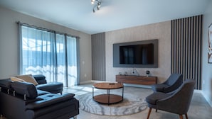 Una sala de estar moderna con un sofá, un sillón, una mesa de centro redonda y un televisor de pantalla plana montado en la pared.