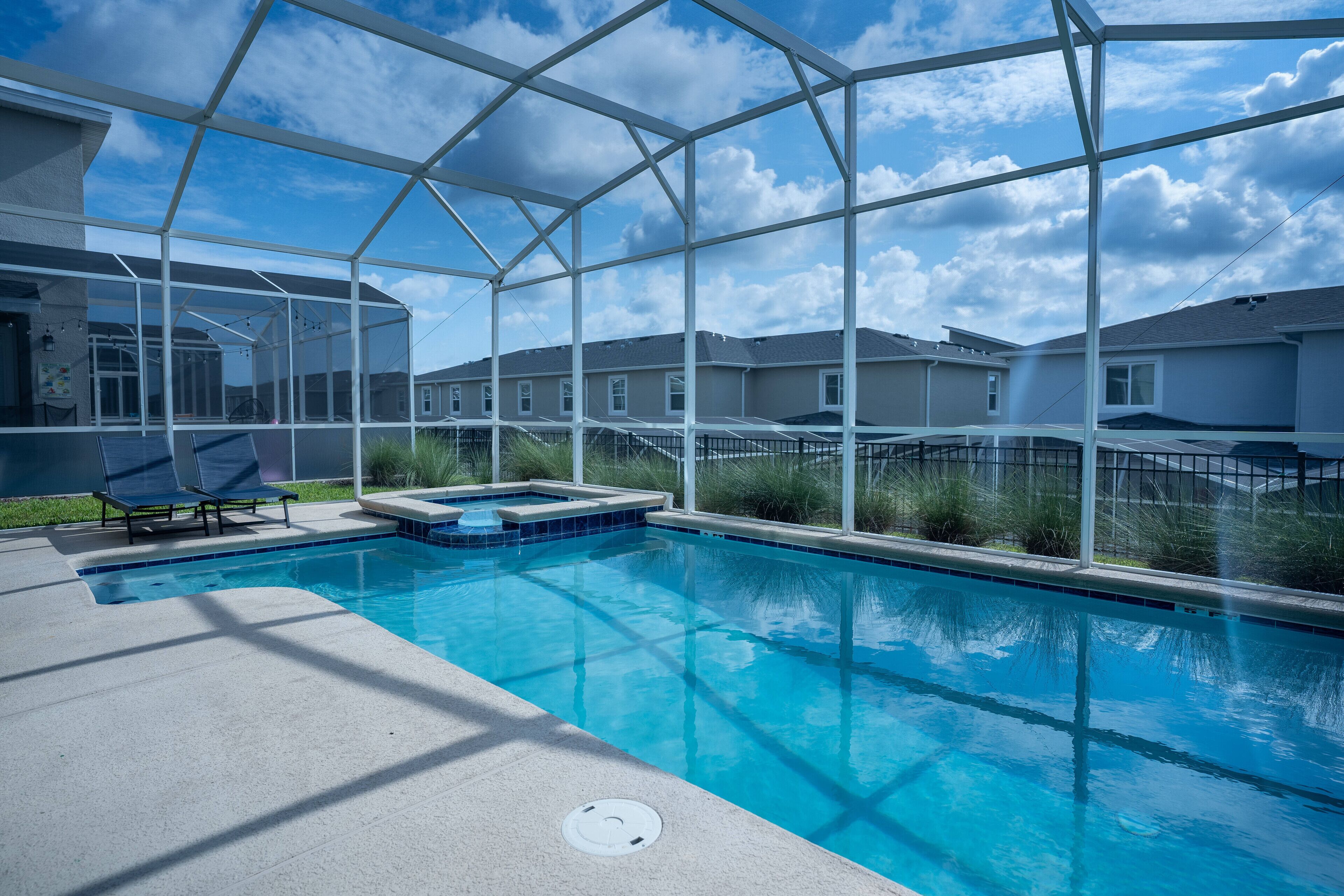 A swimming pool with a glass enclosure, lounge chairs, and a hot tub.