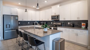Una cocina moderna con armarios blancos, un refrigerador de acero inoxidable, un microondas y una isla central con taburetes de bar.