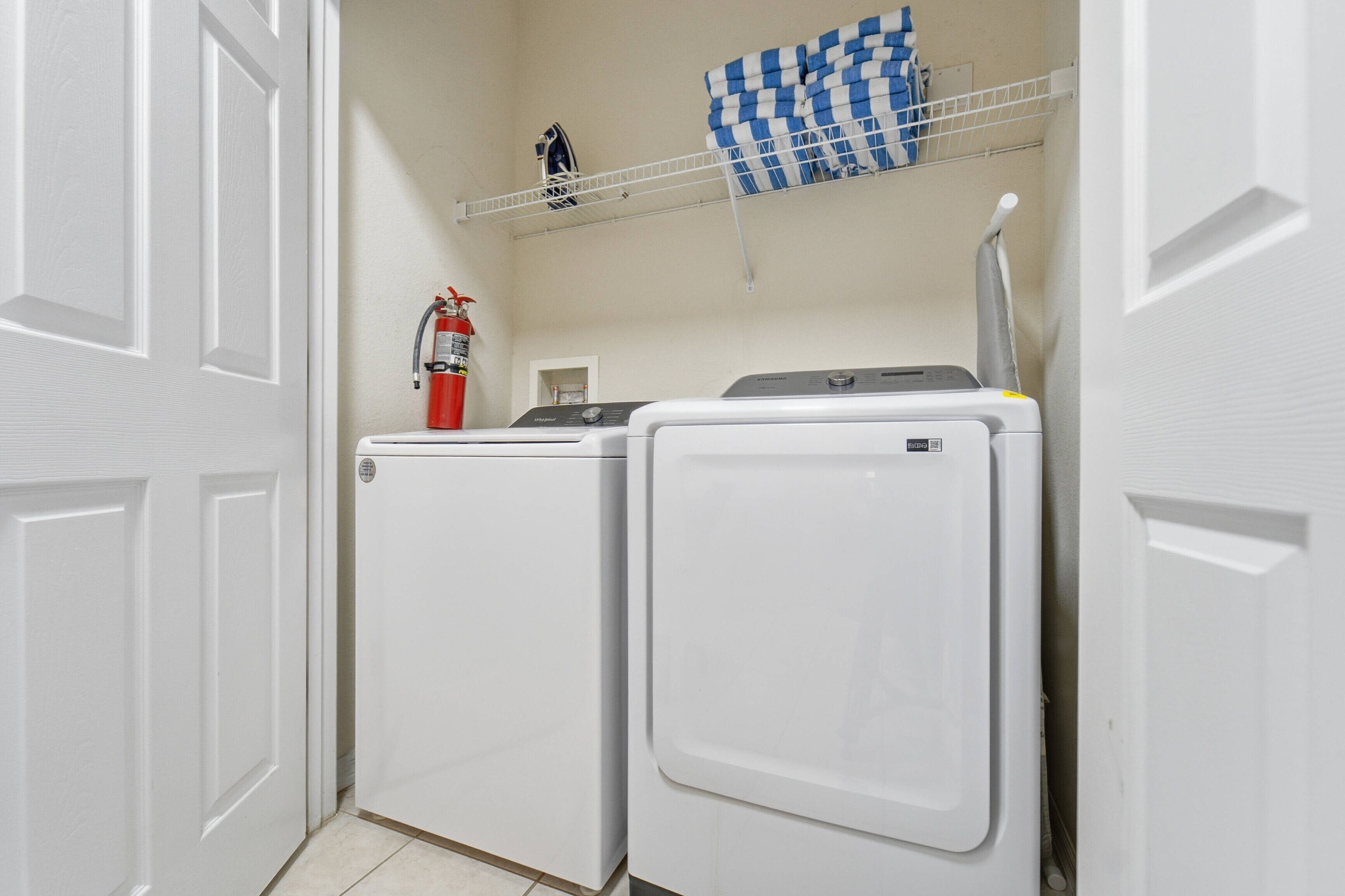 Une buanderie équipée de deux lave-linge et deux sèche-linge blancs, d’un extincteur et d’un tissu à carreaux suspendu à un étendoir.