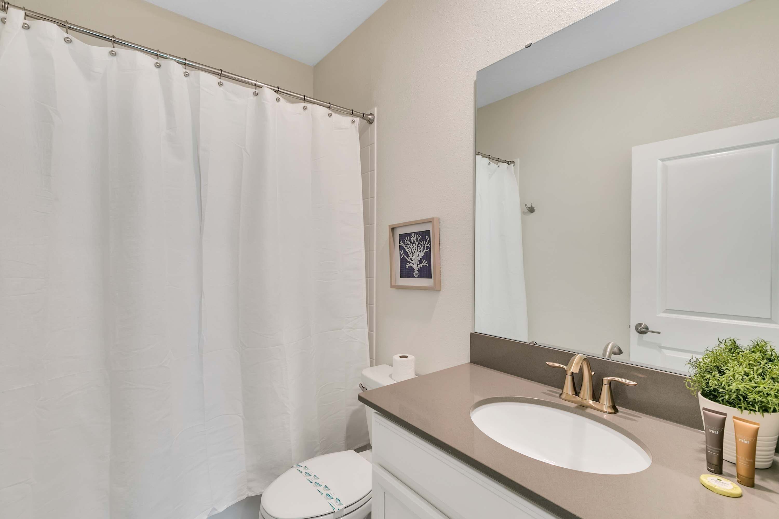 Ein Badezimmer mit Toilette, Waschbecken mit Spiegel darüber und einer Duschvorhang.