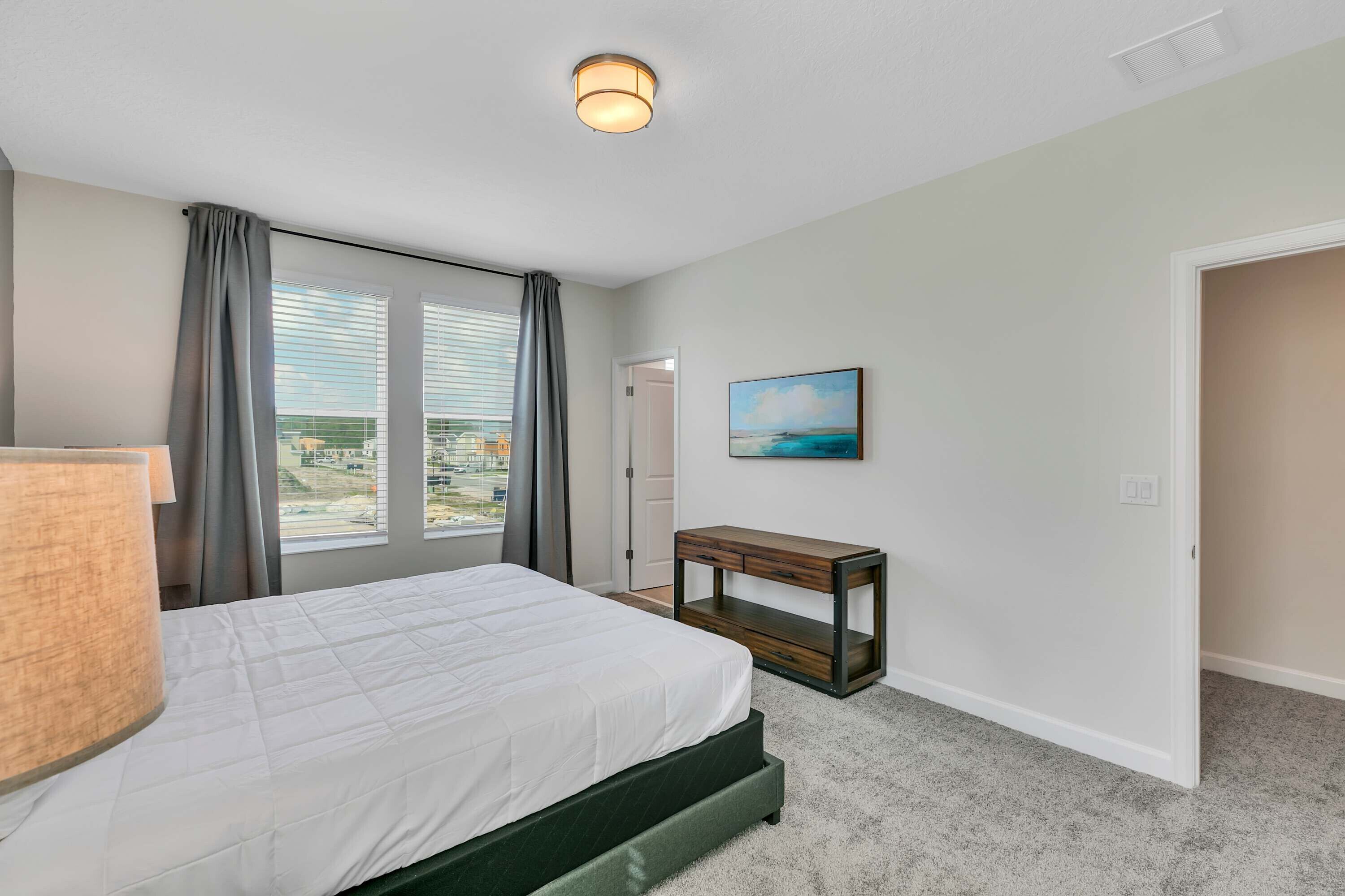 A bedroom with a bed, a nightstand, a painting, and a window with curtains.