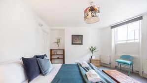 A bedroom with a bed, a blue blanket, a wooden bench, a chair, a plant, and a ceiling light. - Stunning Period Character Courtyard Coastal Flat - Pass the Keys (Hove)
