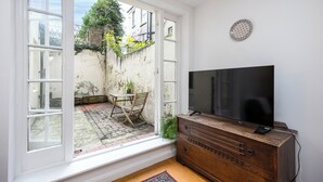 A room with a large window, a wooden dresser, a flat-screen TV, and a small table with chairs. - Stunning Period Character Courtyard Coastal Flat - Pass the Keys (Hove)
