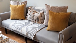 Un canapé gris avec deux coussins de couleur moutarde et un plaid à motifs.