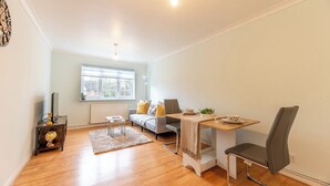 Un salon moderne comprenant un canapé, une table à manger avec une chaise, une petite table d’appoint, un globe terrestre et une fenêtre avec des stores.