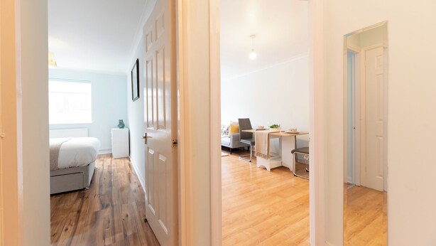 Un couloir avec un lit, un bureau et une chaise, dans une pièce au plancher en bois et aux murs blancs.