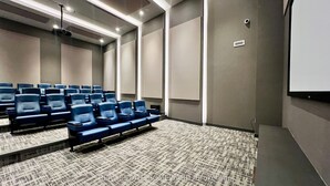 A conference room with rows of blue chairs, a projector screen, and a carpeted floor.