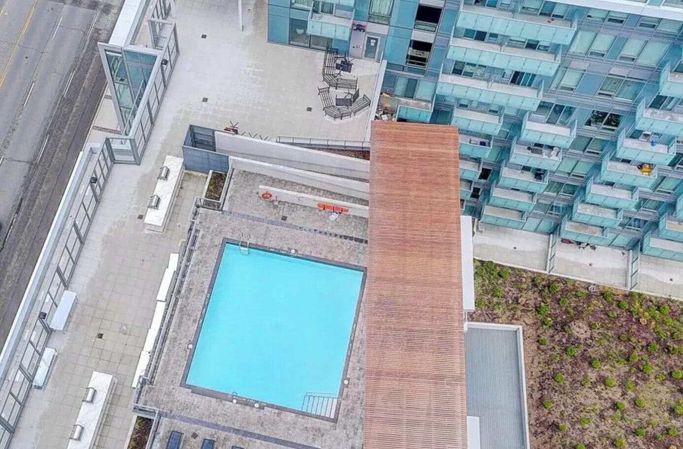 Un edificio de gran altura con piscina en la azotea, junto a un moderno edificio residencial con balcones.