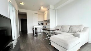 A modern living room with a grey sofa, a small dining table, and a kitchen in the background.