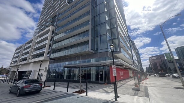A modern multi-story building with a glass facade, a pedestrian walkway, and a car parked on the street.