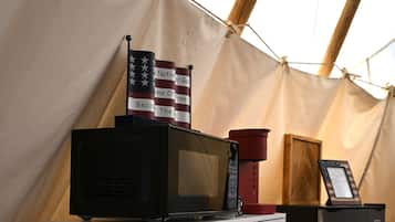 A kitchenette area with a microwave, a coffee maker, and a small refrigerator. There is a flag with text on it and a wooden structure in the background.
