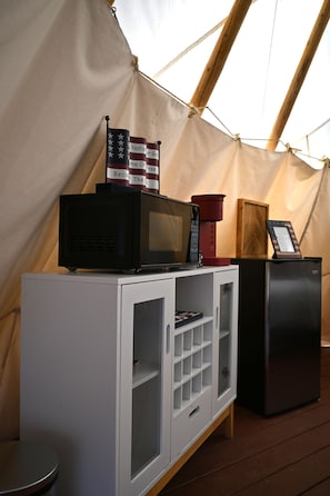 A kitchenette area with a microwave, a coffee maker, and a small refrigerator. There is a flag with text on it and a wooden structure in the background. - Free Bird Teepee at The Edge—Unique Riverfront Glamping in Salt Lick, KY (Salt Lick)