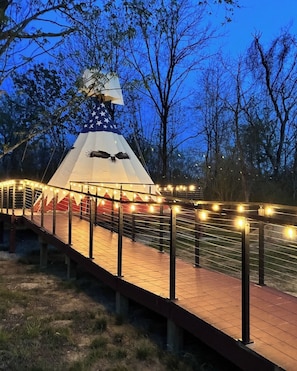 A tent with an American flag and an eagle, surrounded by string lights and a wooden walkway. - Free Bird Teepee at The Edge—Unique Riverfront Glamping in Salt Lick, KY (Salt Lick)