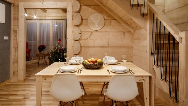 Une salle à manger en bois avec une table dressée pour deux personnes, un sapin de Noël et un escalier.