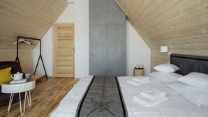 Une chambre avec un plafond en pente, un lit recouvert de draps blancs, une table de chevet avec une lampe et une armoire en bois.