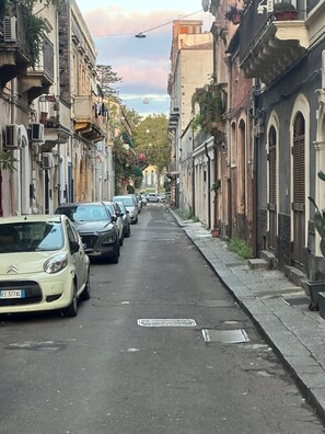 Eine enge Straße, gesäumt von parkenden Autos und historischen Gebäuden mit Balkonen und Klimaanlagen.
