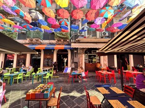 An outdoor café with colorful umbrellas, green and red chairs, and tables with menus. - Spazio Apartments Fornai (Catania)