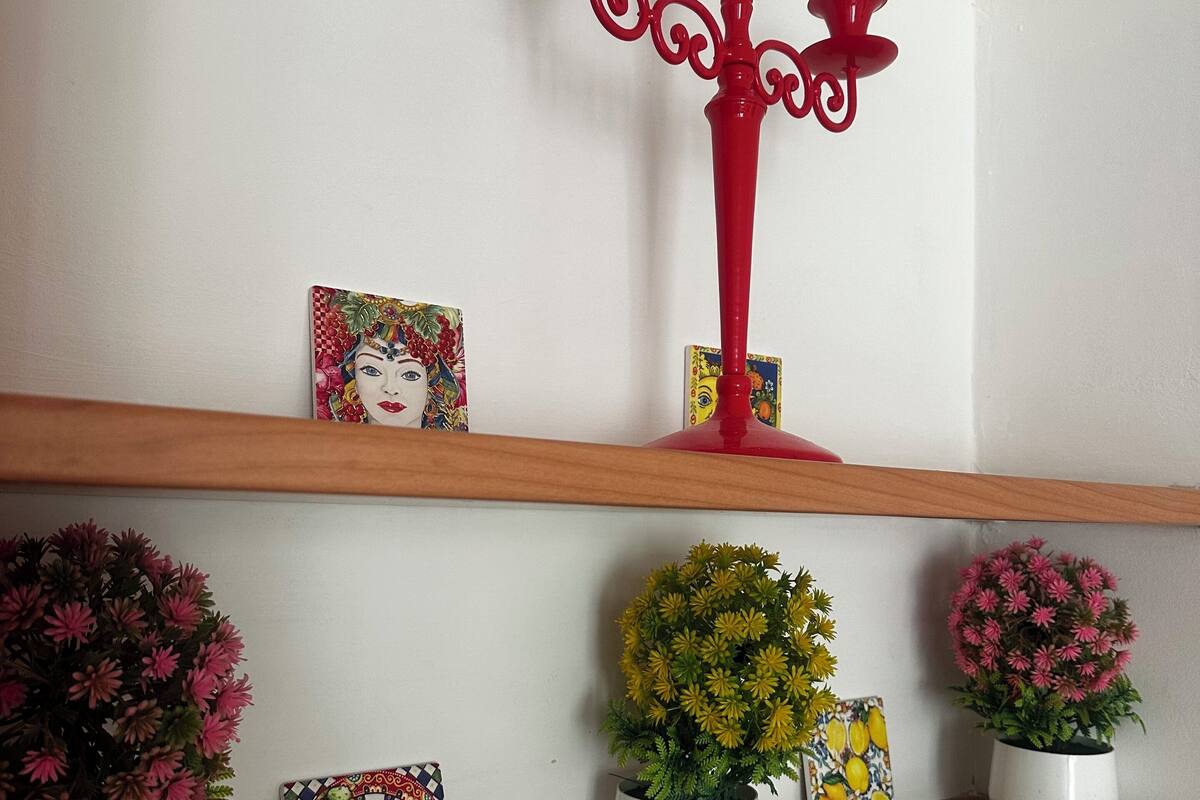 Une étagère ornée d’objets décoratifs, notamment un chandelier rouge, des œuvres d’art encadrées et des plantes en pot.
