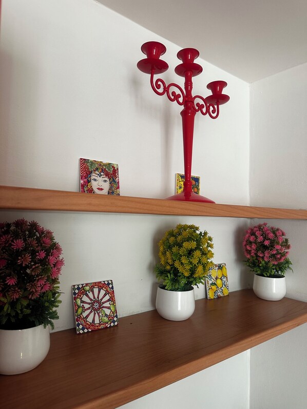 Ein Regal mit Dekorationsobjekten, darunter ein roter Kerzenleuchter, gerahmte Kunstwerke und Topfpflanzen.