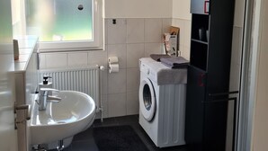 A modern bathroom with a white sink, a washing machine, and a black cabinet. - Trade fair/holiday accommodation (Willich)