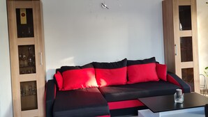 A modern living room with a black and red sectional sofa, wooden cabinets, and a wall clock. - Trade fair/holiday accommodation (Willich)