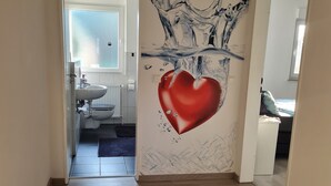 A hallway with a wooden floor, a bathroom with a white sink and toilet, and a bedroom with a bed and window. - Trade fair/holiday accommodation (Willich)