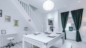A modern kitchen with white cabinetry, a dining table set for four, and a staircase leading to an upper level. - Modern 2 - Bed House Near Manchester City Centre - Sleeps 6 (Salford)