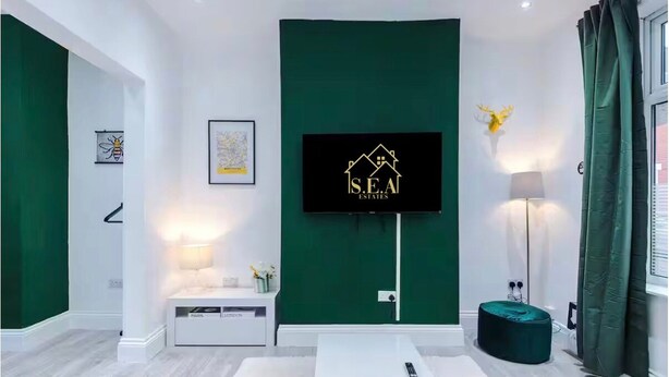 A modern living room with a mounted TV, a green accent wall, a white sofa, a floor lamp, and a decorative deer head. - Modern 2 - Bed House Near Manchester City Centre - Sleeps 6 (Salford)