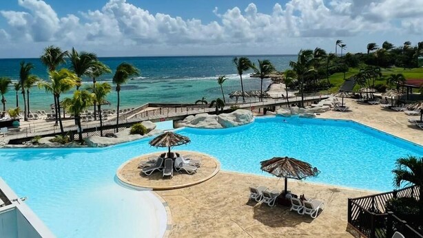 Piscina di un resort con vista sull'oceano, circondata da palme e poltrone relax.