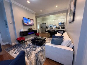 Een moderne woonkamer met een flatscreen televisie, een open haard en een eethoek, met een keuken op de achtergrond.