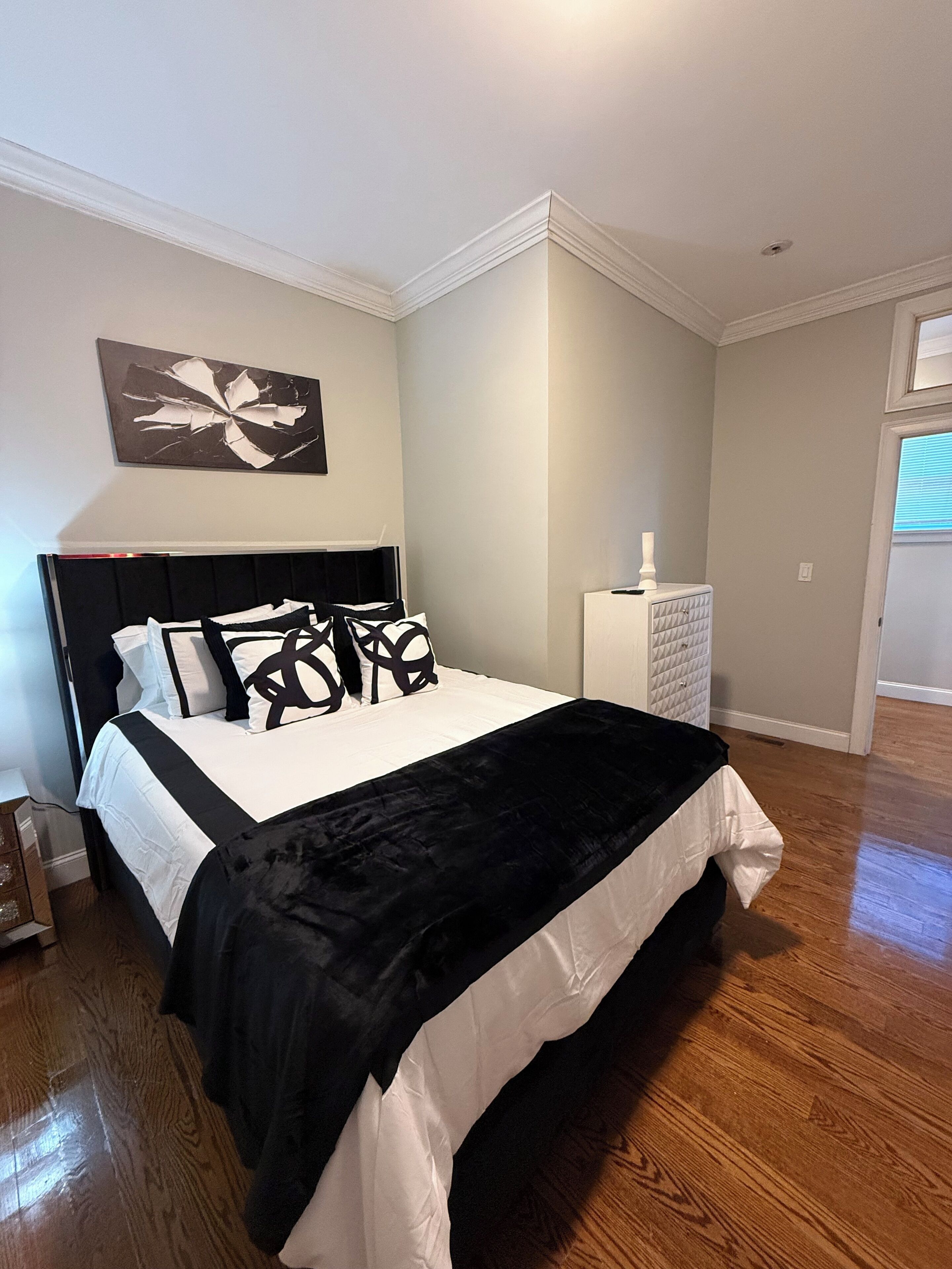 A bedroom with a large bed, a nightstand, a dresser, and a wall-mounted artwork.