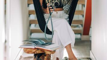 A person sitting in a hammock in a hallway with wooden beams, holding a camera.