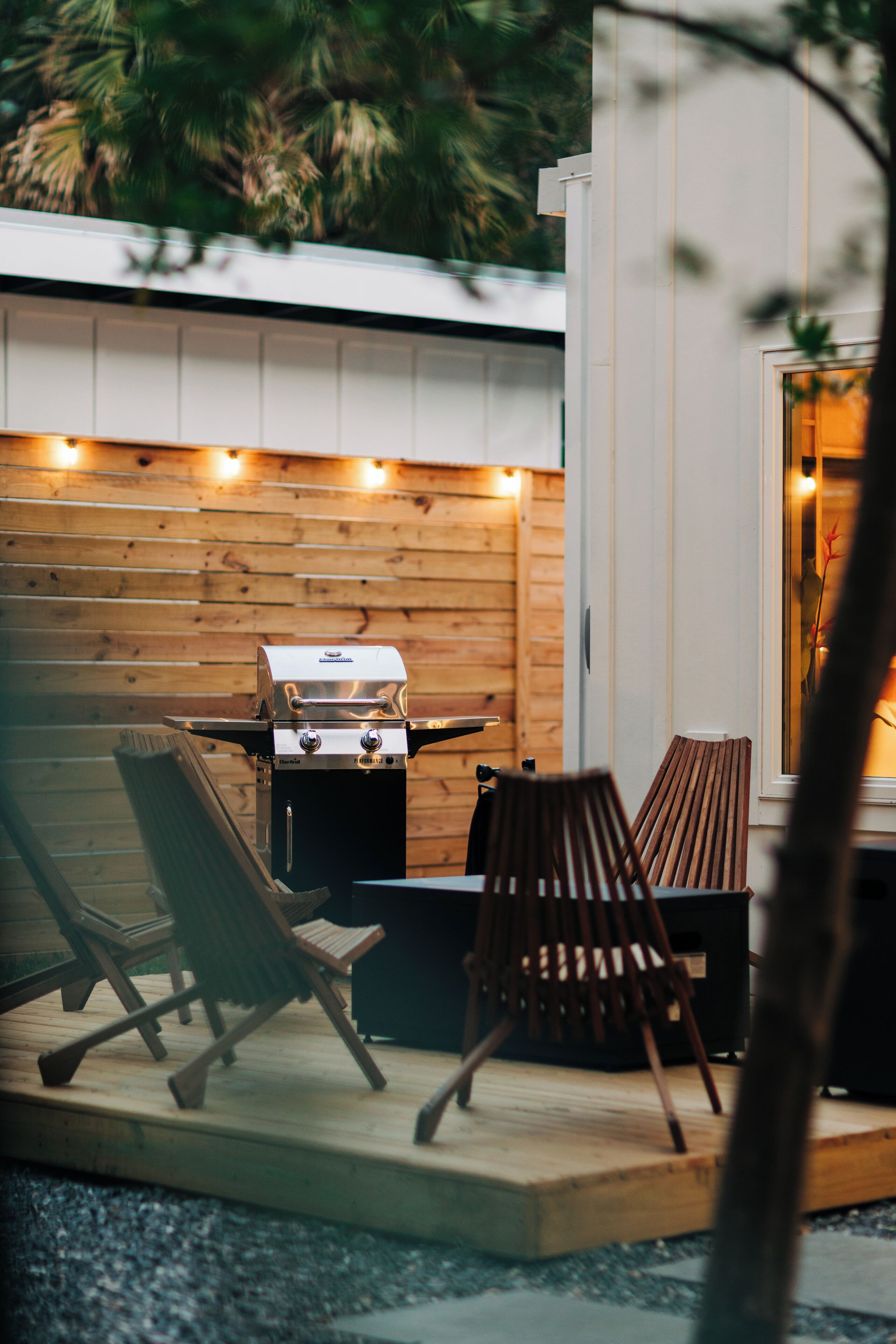 An outdoor patio with a grill, wooden chairs, and a table.